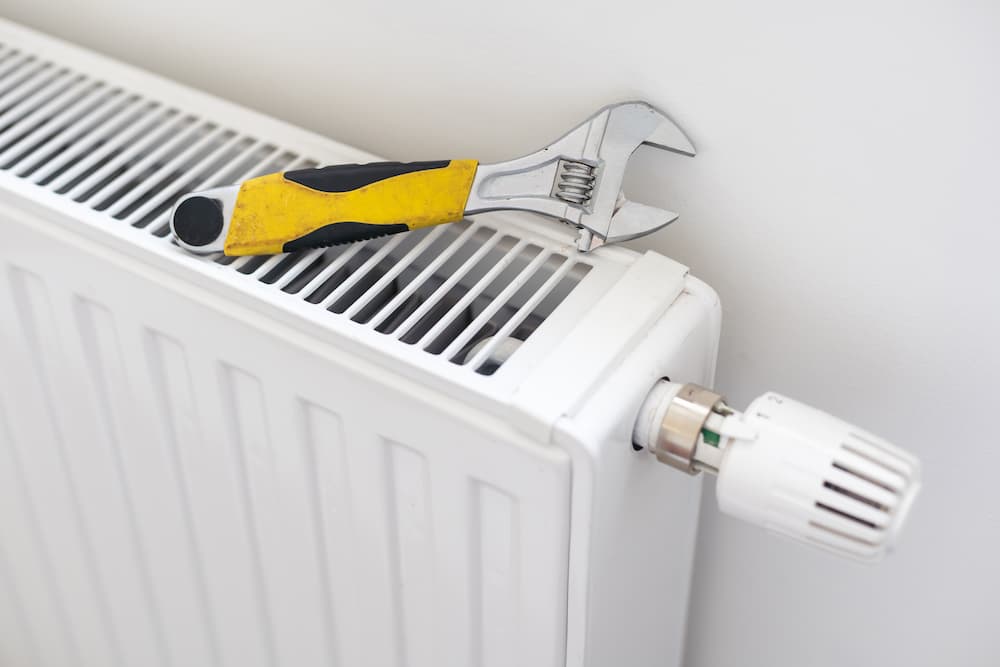 An adjustable wrench resting on top of a white residential radiator, illustrating how to fix cold spots in a house and optimize home heating efficiency.