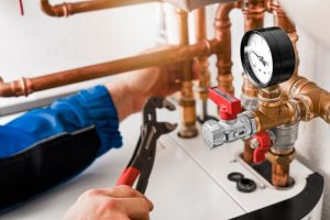 A technician using a wrench to adjust copper pipes on a residential boiler, illustrating professional HVAC systems maintenance and how to repair a heating system.